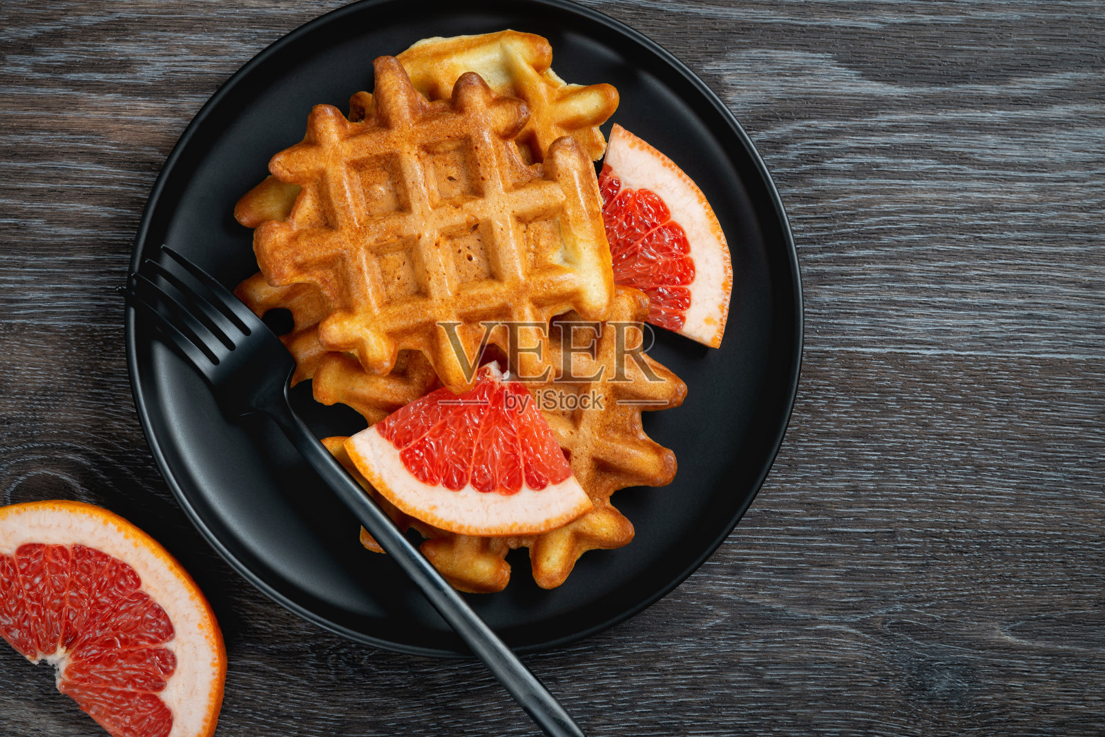 华夫饼和葡萄柚放在木桌上的黑盘子里照片摄影图片