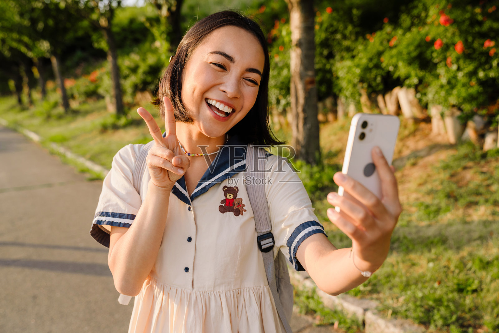 开朗的亚洲女孩用智能手机视频通话，站在公园里挥手照片摄影图片