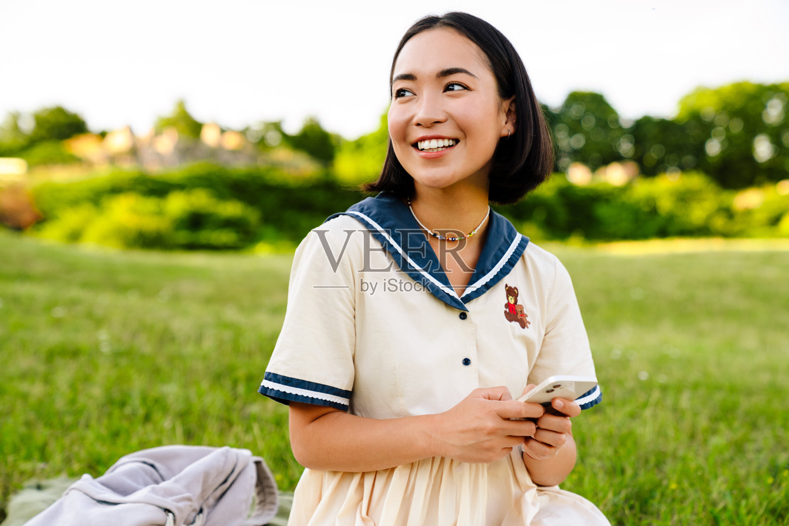 年轻的亚洲女孩坐在绿色公园里用手机照片摄影图片