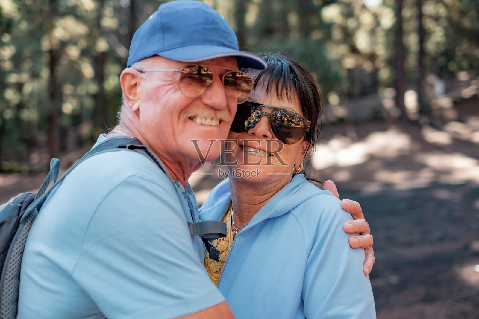 微笑的白人夫妇拥抱在树林里看着相机。有魅力的老年人享受健康的生活方式，徒步登山照片摄影图片