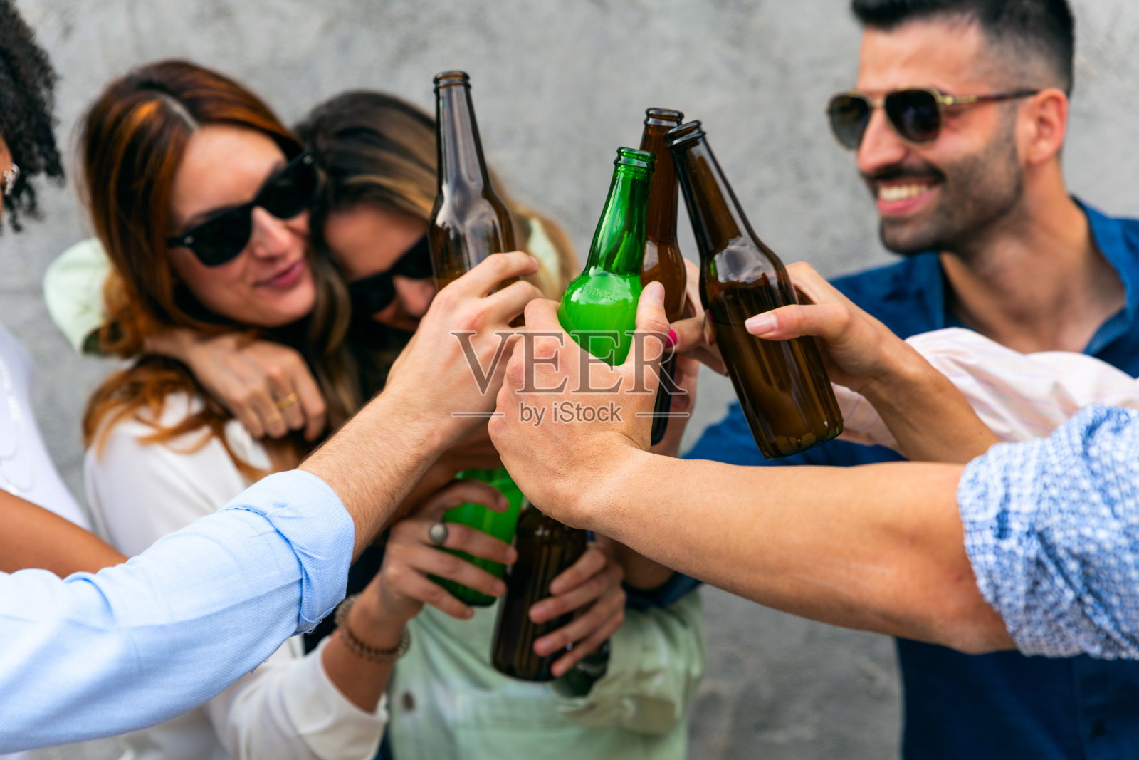 多种族的年轻人用啤酒瓶敬酒。照片摄影图片