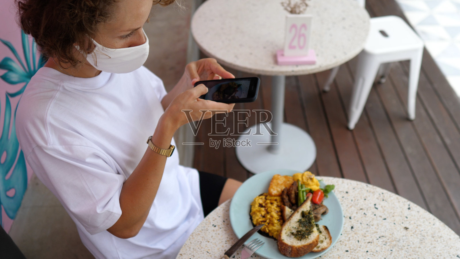 一个白人女博主用智能手机拍她的素食早餐的俯视图。她每天都做一份摄入卡路里的报告。在covid-19大流行期间外出就餐。照片摄影图片