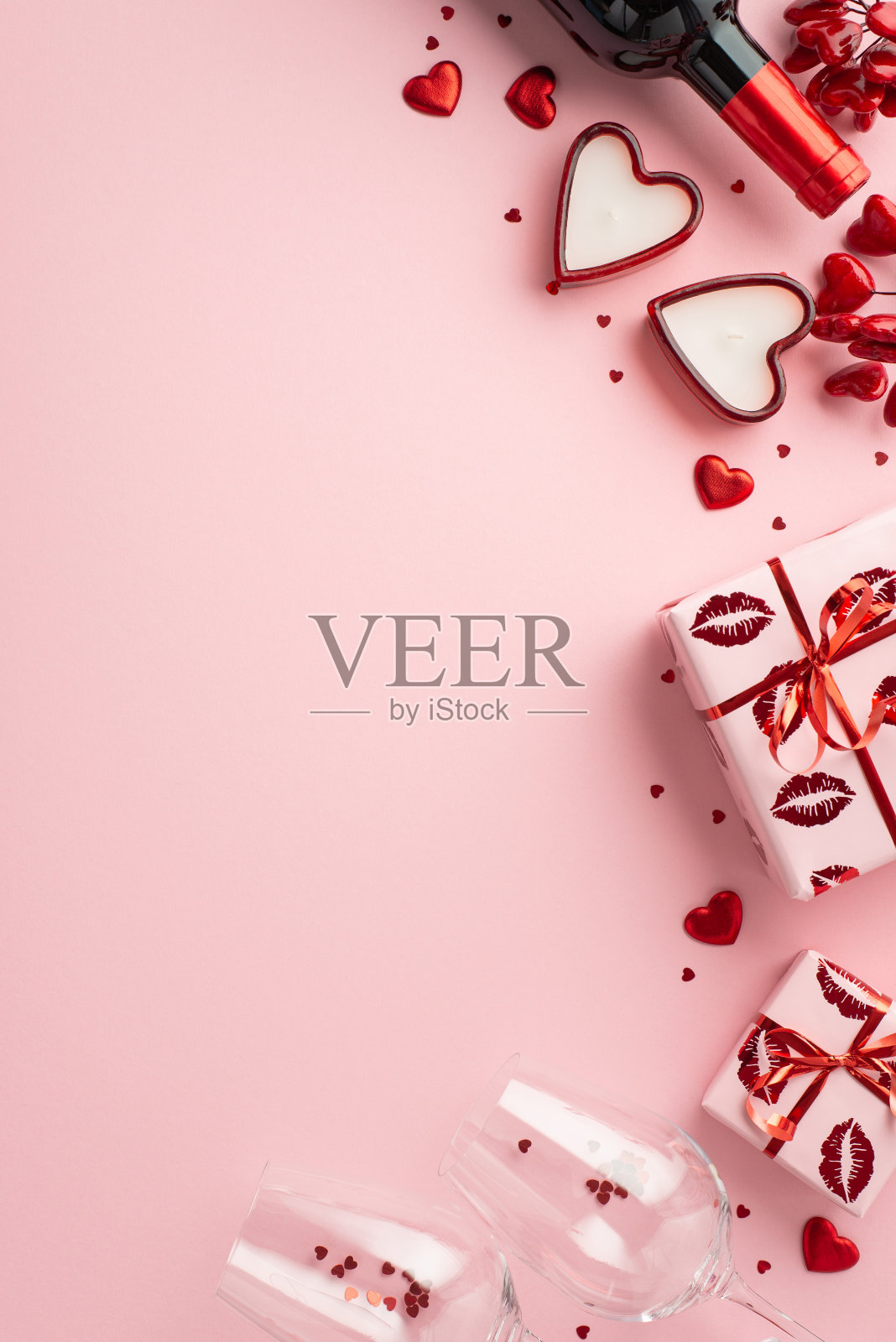 情人节的概念。俯视图垂直照片酒瓶玻璃杯与纸屑礼物盒和心形蜡烛在孤立的粉彩粉红色背景与复制空间照片摄影图片