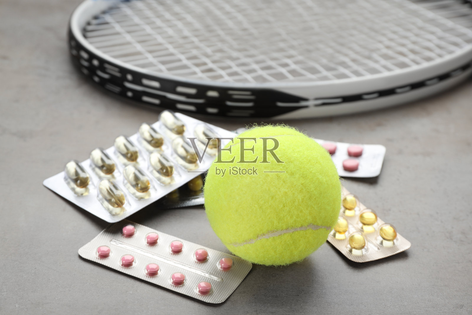 浅灰色的桌子上有网球、球拍和不同的药片，特写。掺杂的概念照片摄影图片
