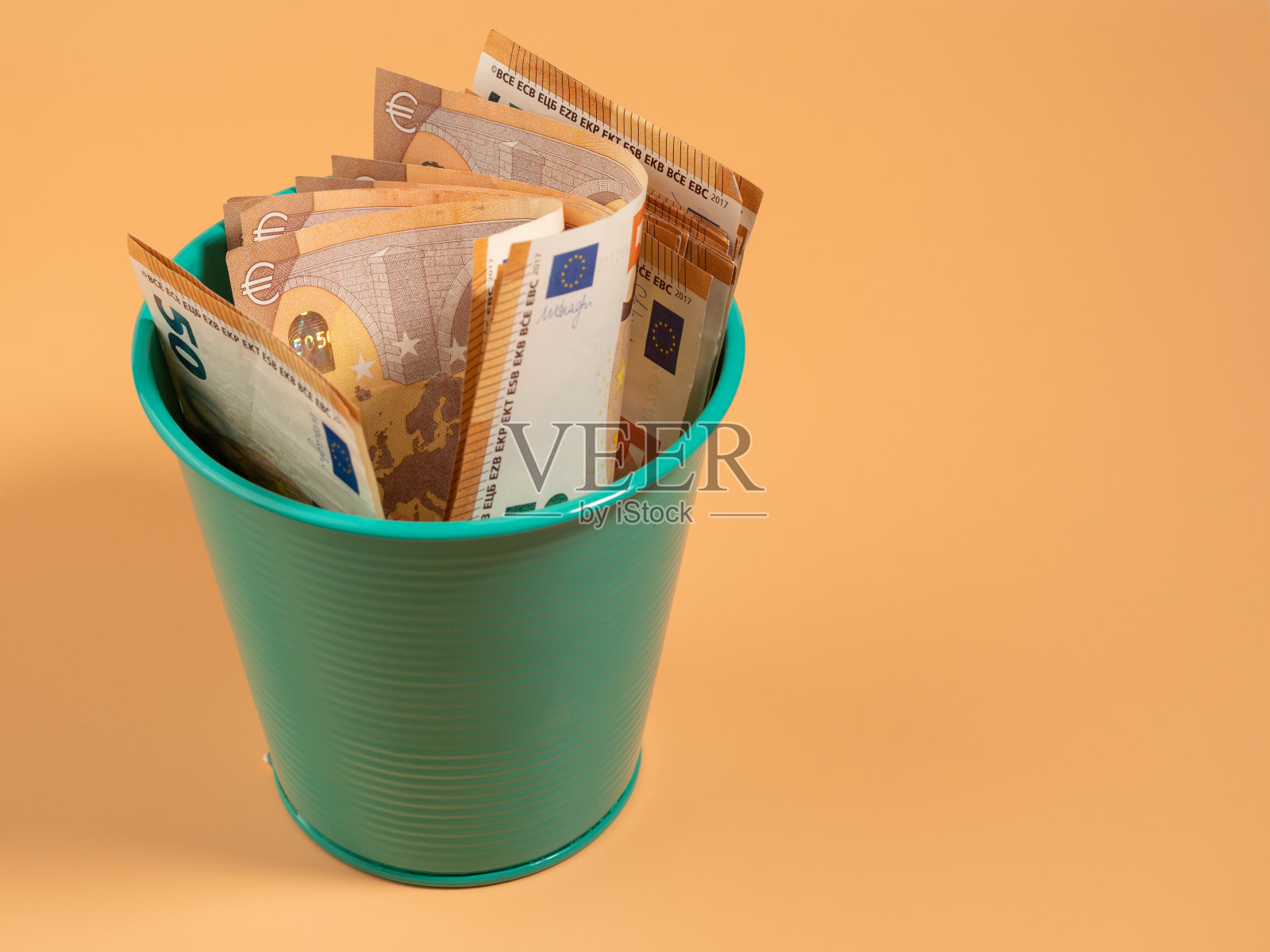 垃圾桶里的钱，背景是橙色的。欧元在垃圾桶里。浪费钱的概念。照片摄影图片