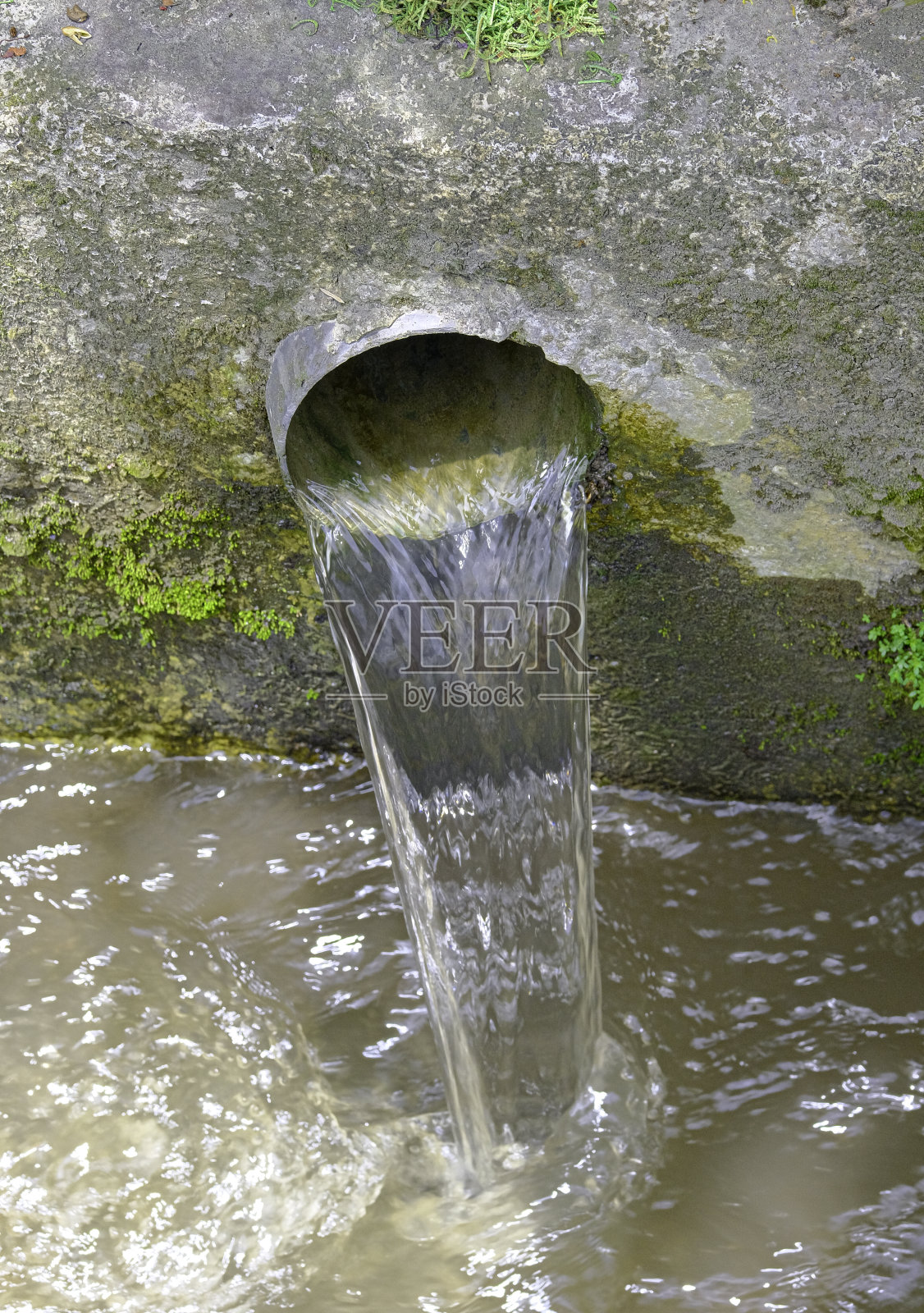 近距离的旧水银色金属管在混凝土墙与水倒进溪流照片摄影图片