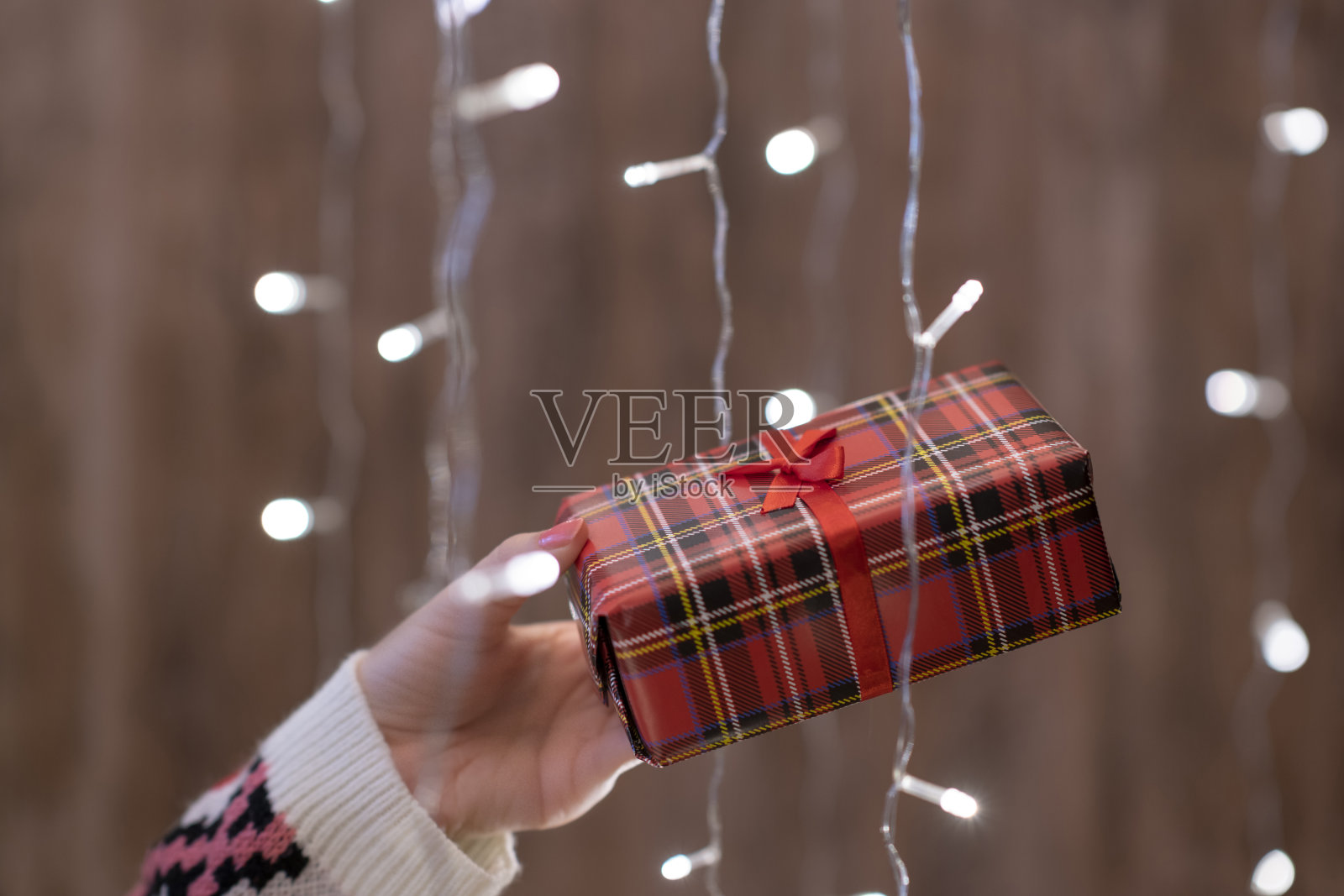 女人的手拿着礼盒透过发光的花环。圣诞节照片摄影图片