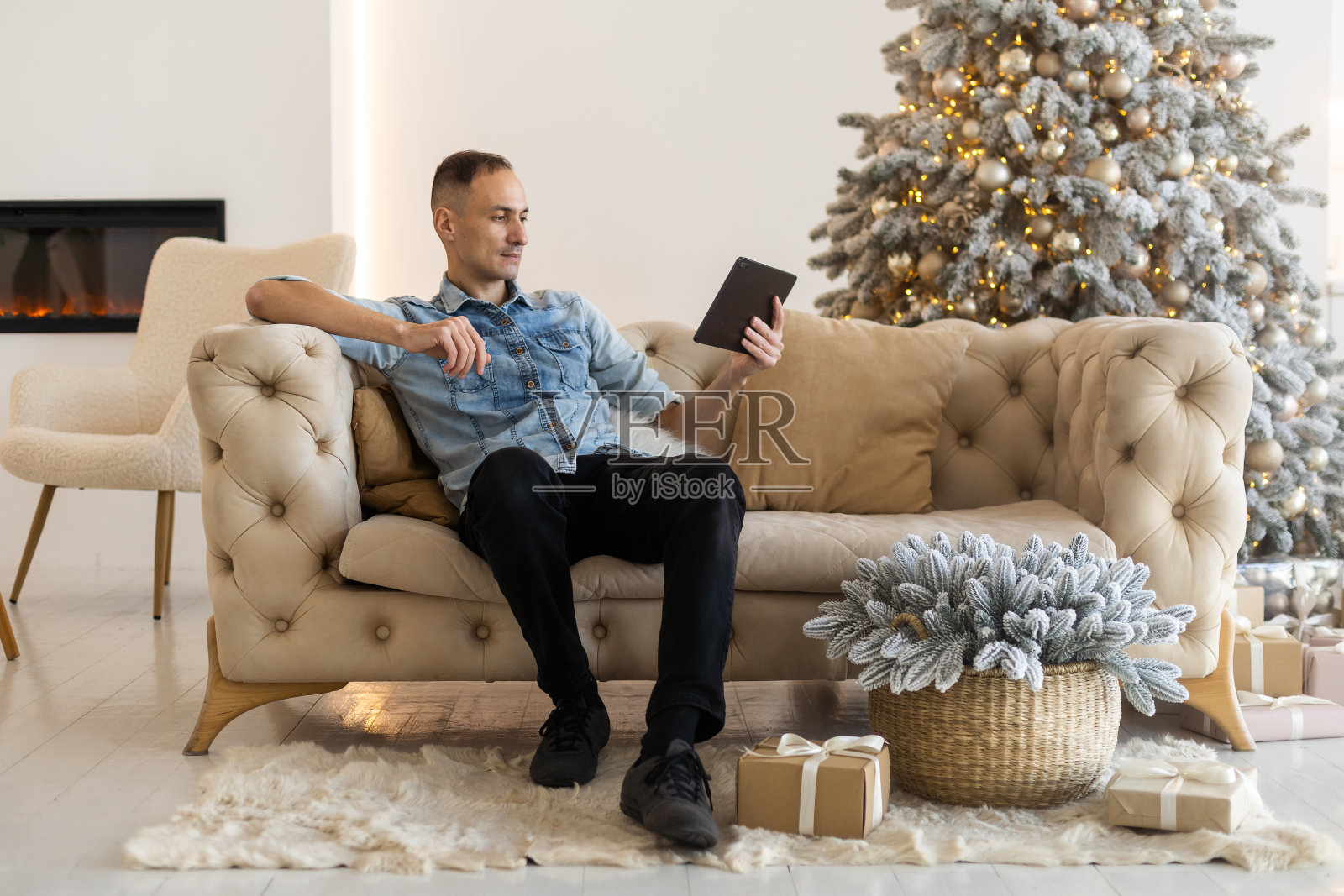 圣诞节期间，年轻男子拿着平板电脑坐在家里的沙发上。他和家人视频通话。照片摄影图片