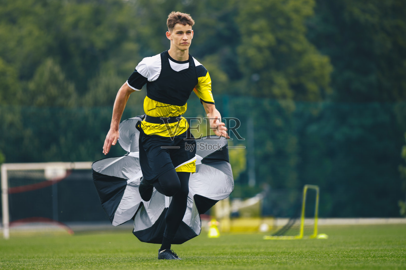 青少年足球运动员在训练期间进行跑步测试。男子足球队队员带着训练降落伞奔跑照片摄影图片