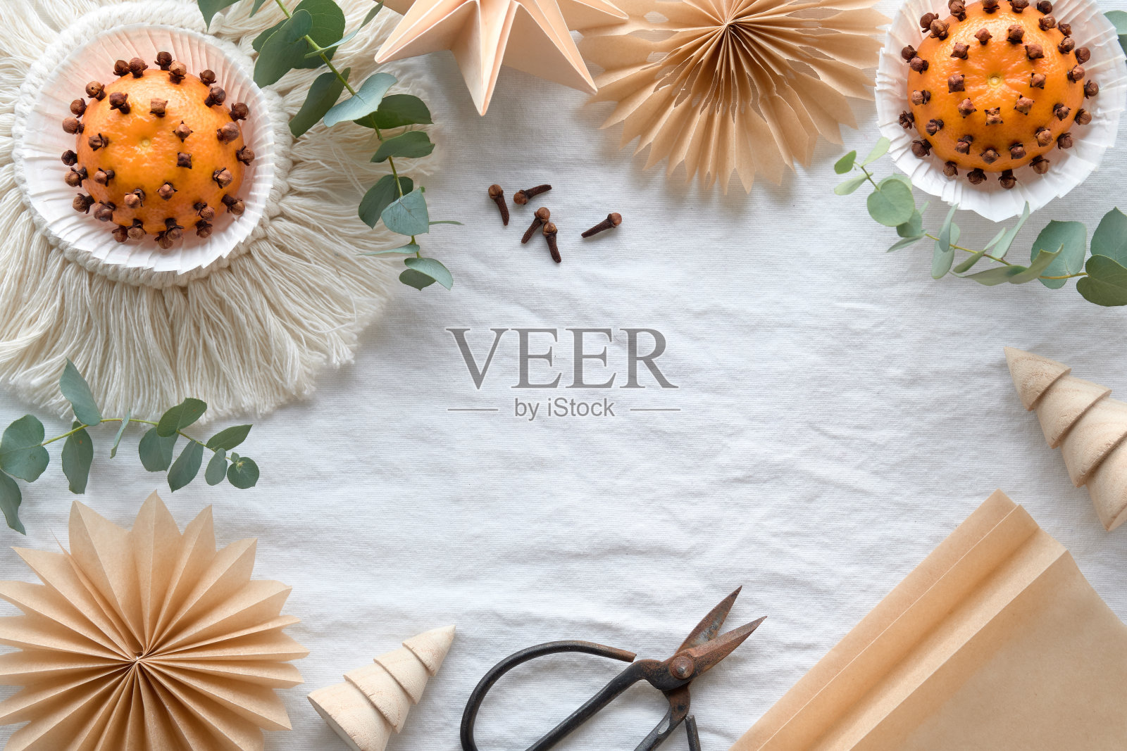 用橘子和丁香手工制作的香精球。用棕色烘焙纸制作的手工纸星星。平铺在白色的纺织台布上，上面有芳香的绿色桉树树枝。照片摄影图片