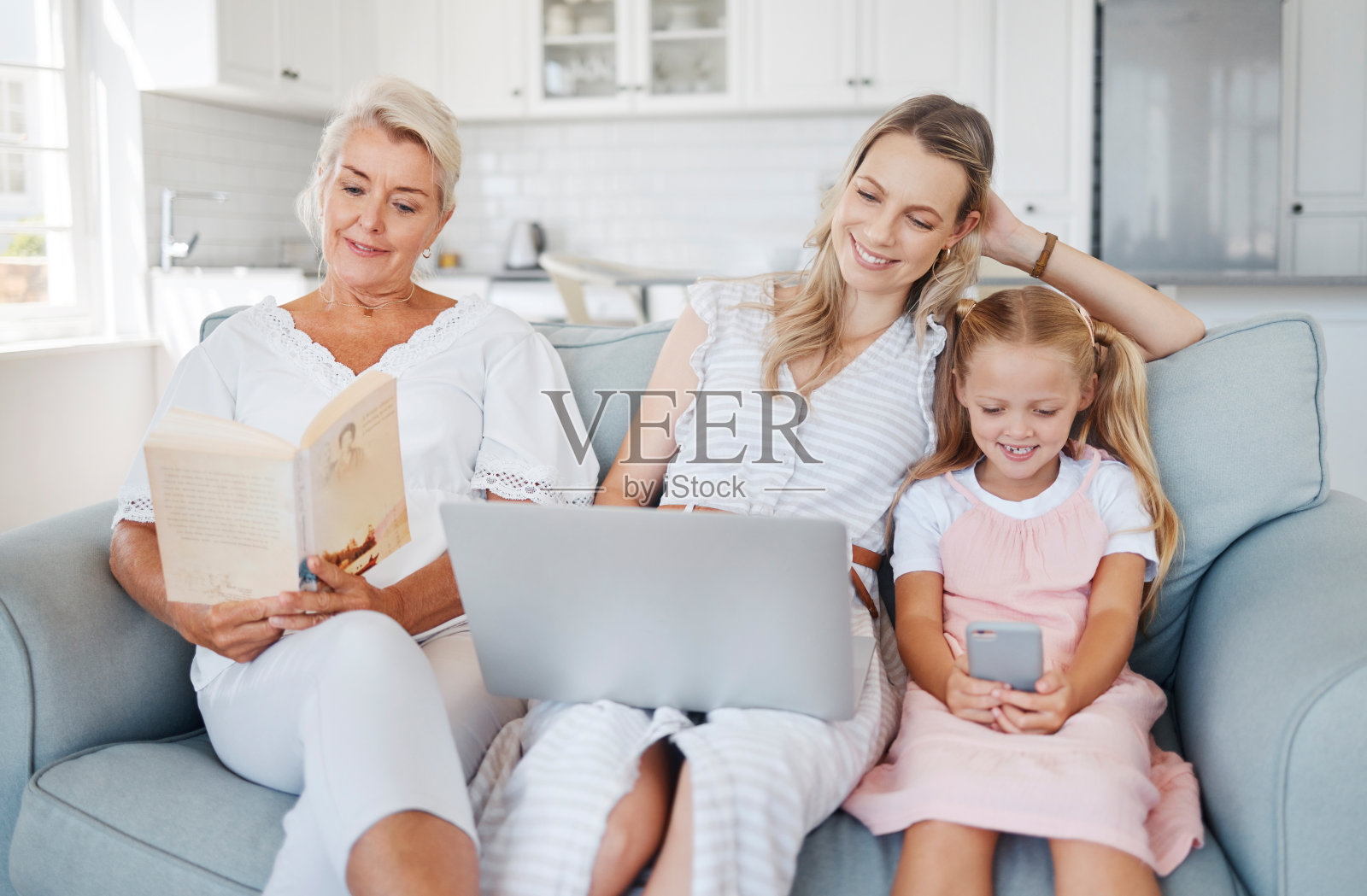 笔记本电脑，手机或书籍与祖母在沙发上享受阅读休闲与家人在舒适的家。放松，在澳大利亚的家庭和客厅活动与快乐的奶奶，妈妈和孩子。照片摄影图片