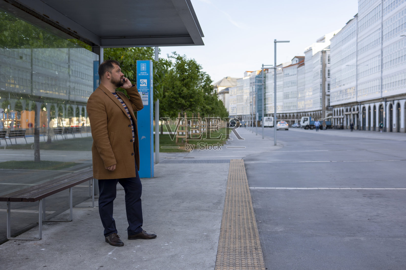 一位商人在公共汽车站边等车边打电话。照片摄影图片