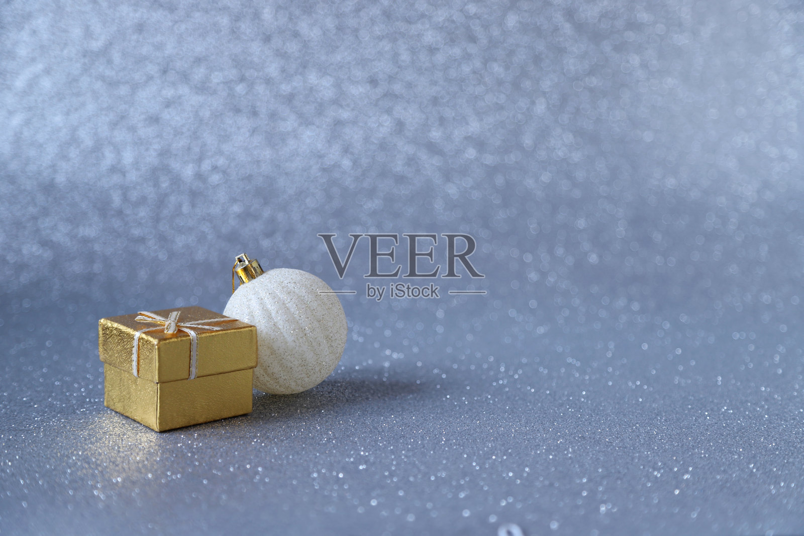 金色的礼品盒和白色的圣诞球装饰在银色闪闪发光的背景。选择性对焦照片照片摄影图片