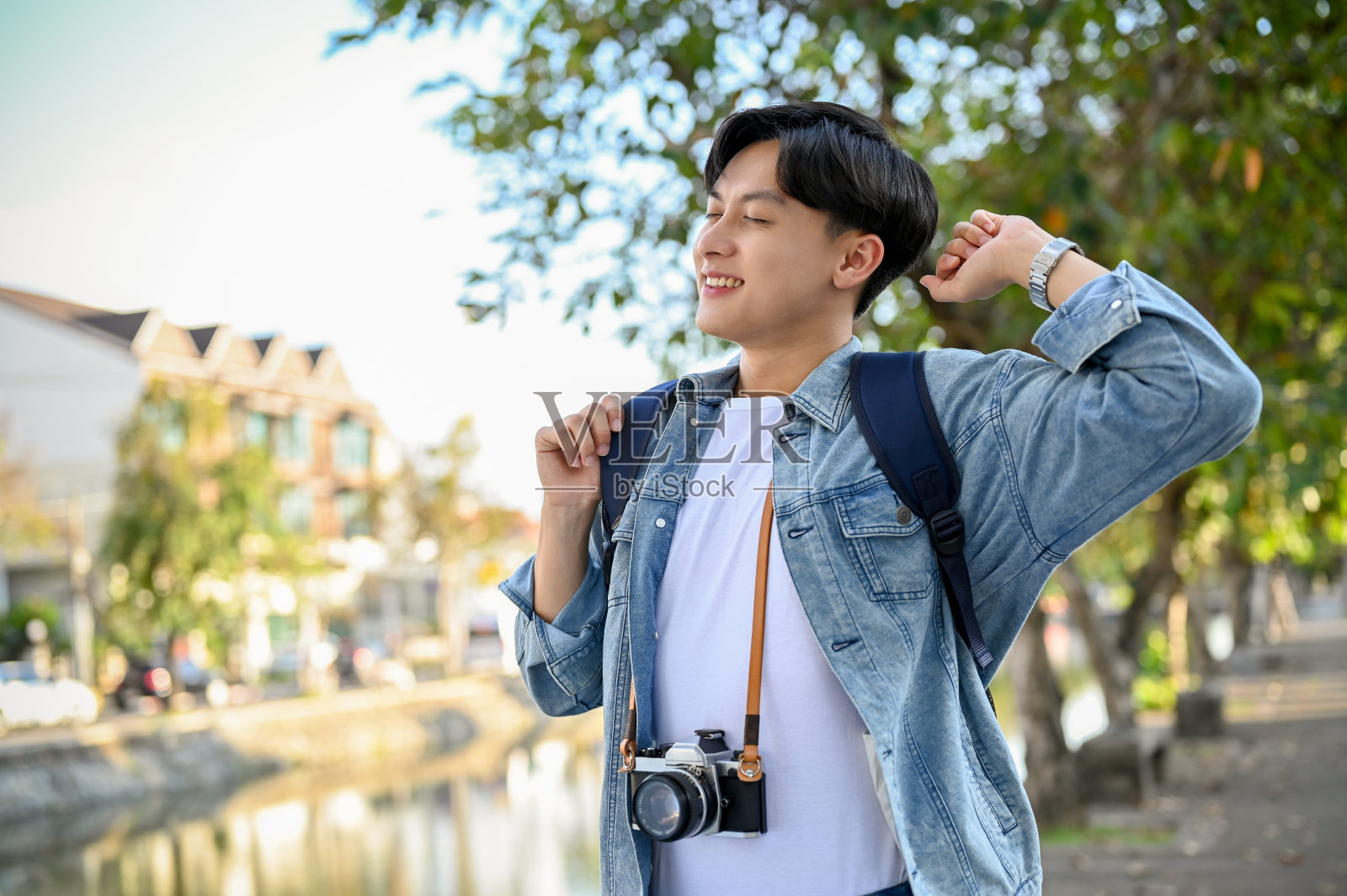 快乐和放松的亚洲男性旅行者与他的相机漫步在城市，享受旅行照片摄影图片