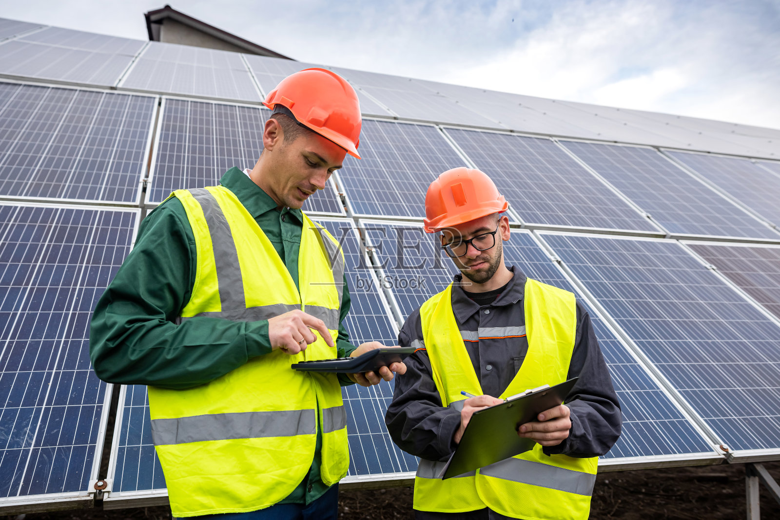穿着特殊衣服的年轻漂亮的工人们写下了安装太阳能电池板的计划。照片摄影图片