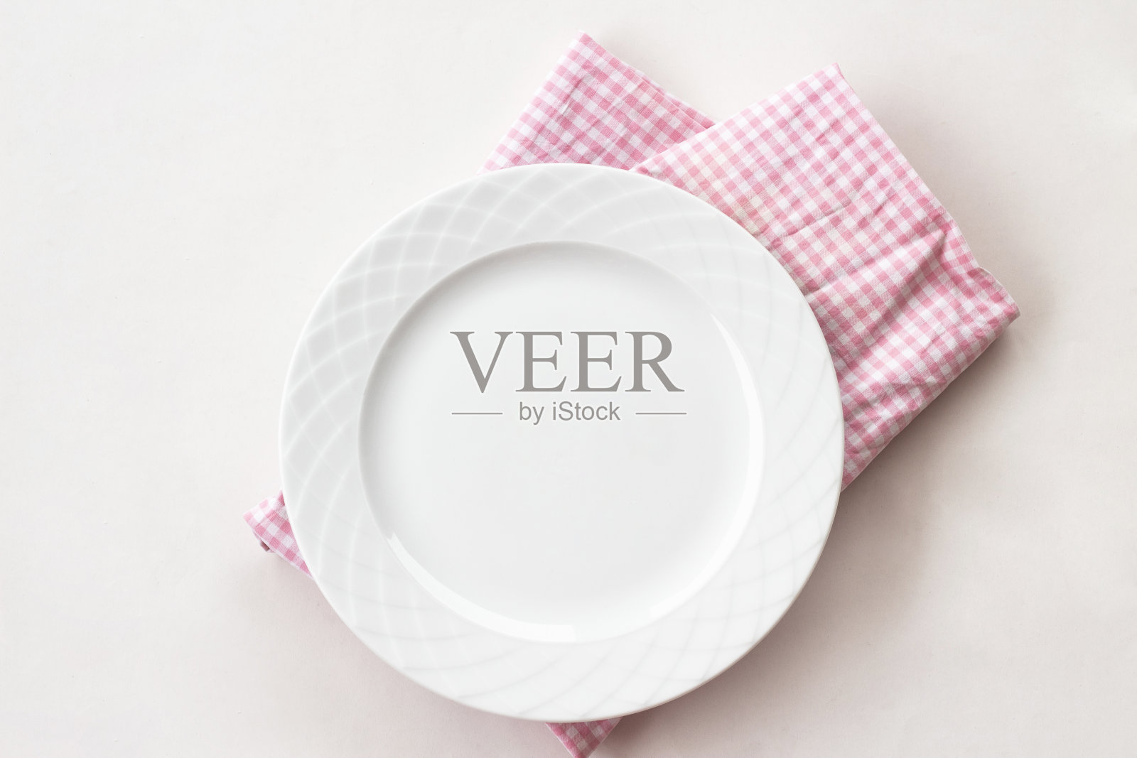 白色的餐桌上放着一个空的白色盘子和粉红色的餐巾，一把叉子和一把刀。前视图。照片摄影图片