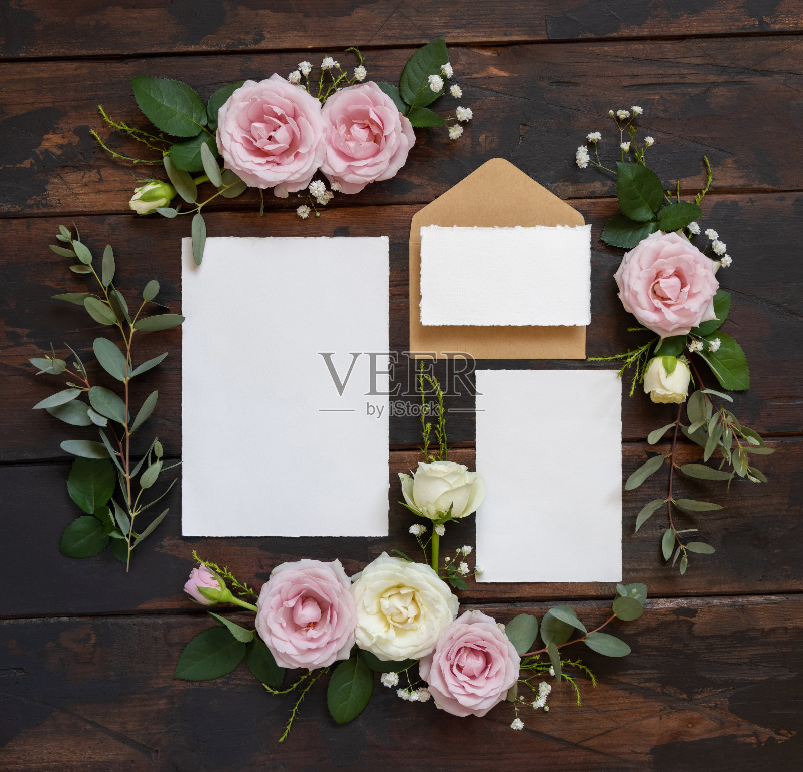 卡片和信封之间的粉红色和奶油玫瑰在棕色的木材顶部视图，婚礼的模型照片摄影图片
