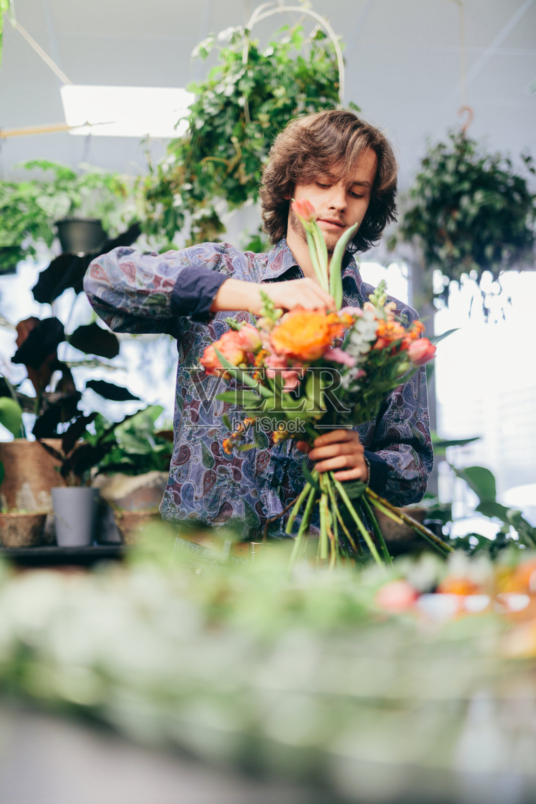 年轻男子在花店整理花束。照片摄影图片