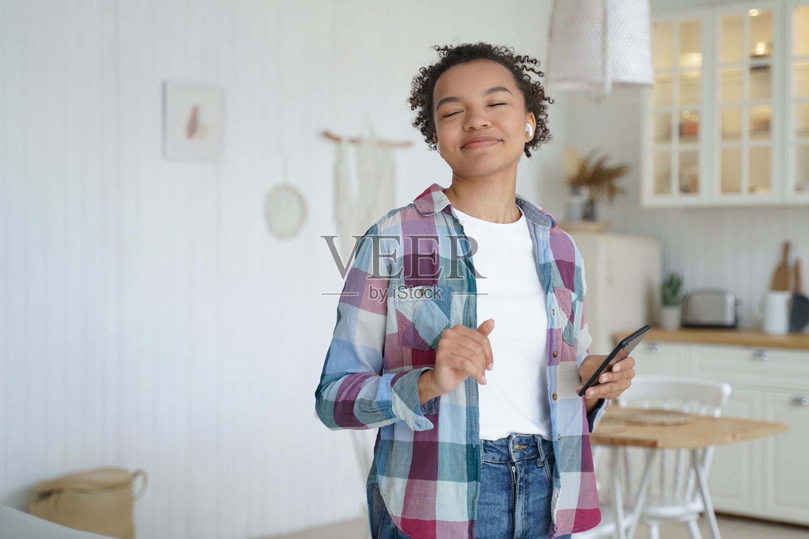 混血儿小女孩听音乐，享受声音使用音乐应用程序在手机上在家里照片摄影图片