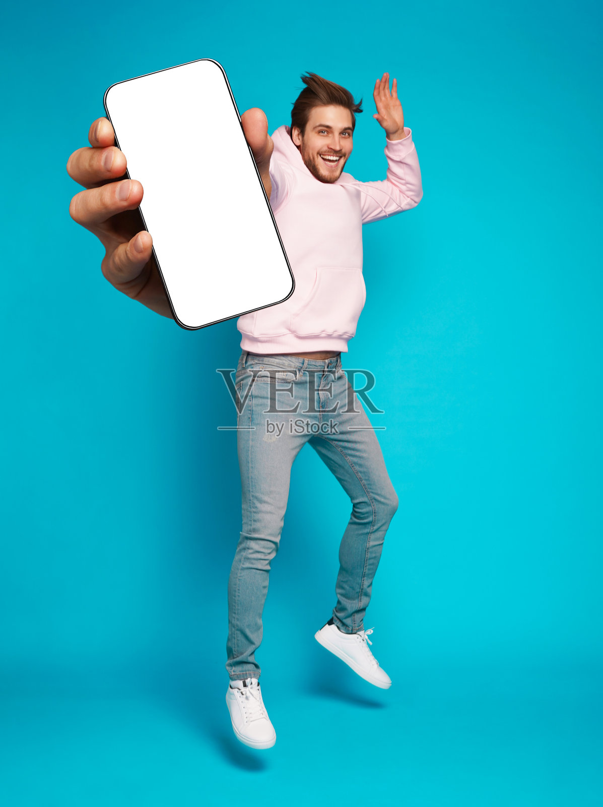 英俊兴奋的男子指着空的智能手机屏幕在浅蓝色背景上摆姿势，对着相机微笑照片摄影图片