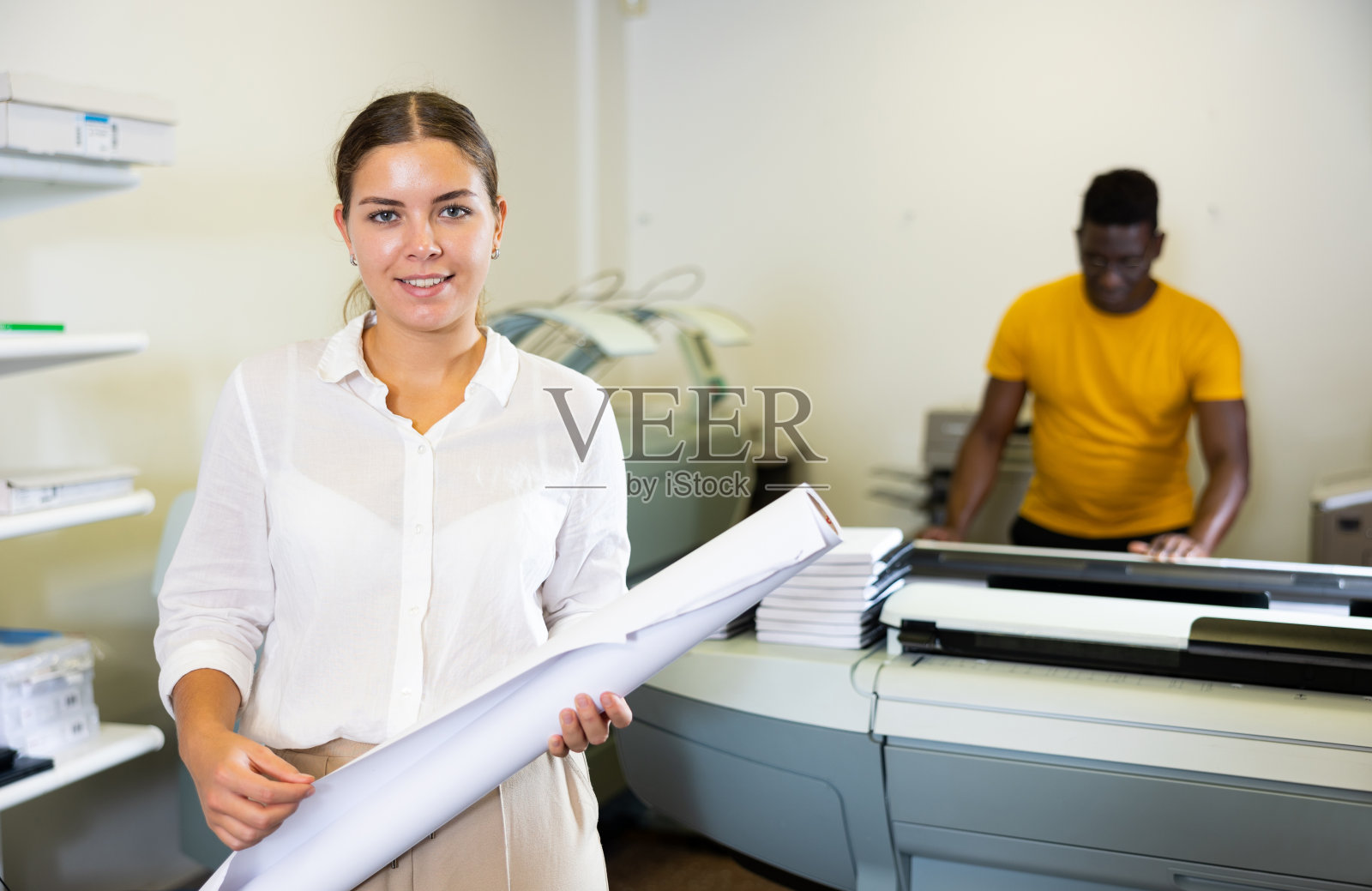 快乐的年轻女性专家在白衬衫拿着什么人在一卷印刷照片摄影图片