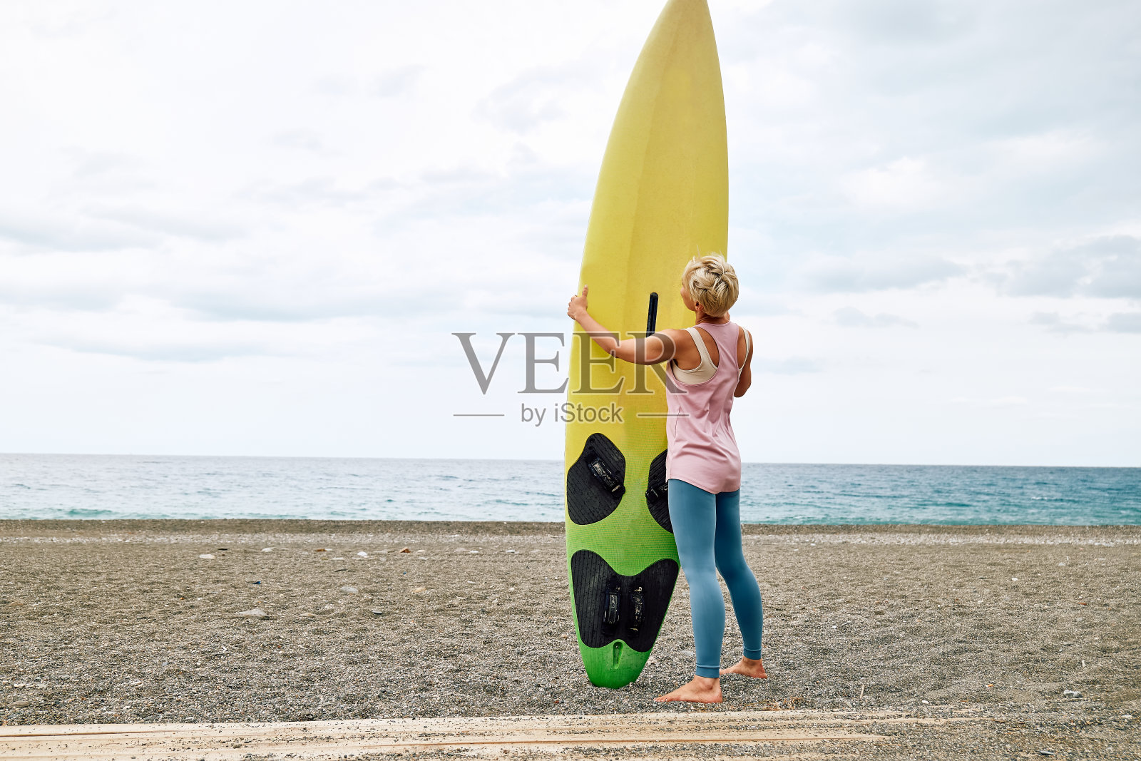 年轻的金发女子冲浪者在阴天的海滩上冲浪板。极限运动，水上运动概念。照片摄影图片