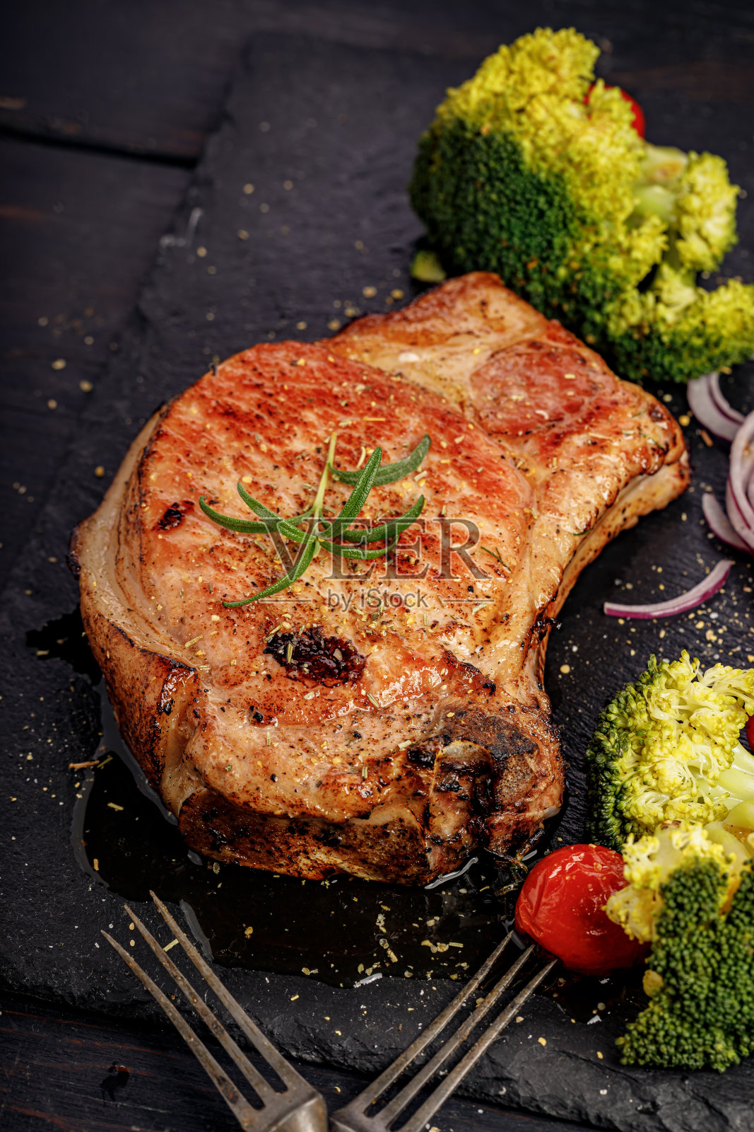 开胃的烧烤猪腰肉和蔬菜在一个黑色的石板。烤猪肉和西兰花。垂直拍摄。古老的乡村木制背景照片摄影图片