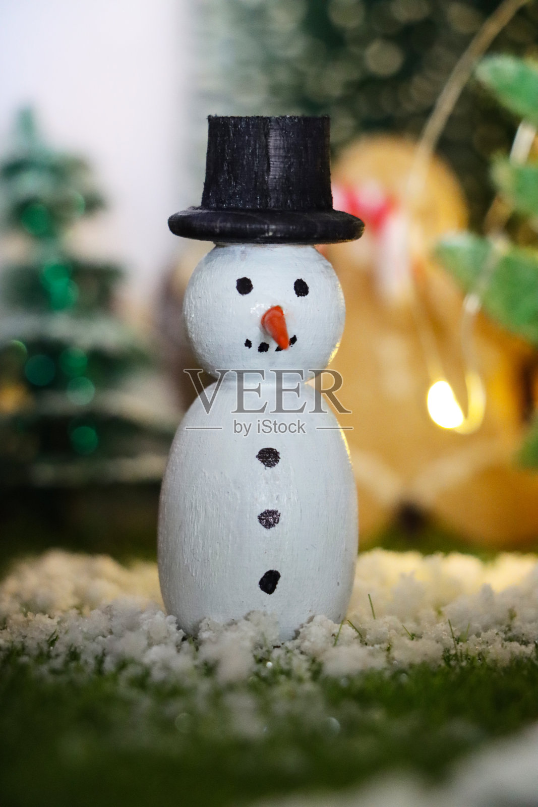 特写图像的木制雪人节日自制圣诞装饰在风景圣诞村展示在橱柜顶部，人造塑料圣诞树，照明自制木屋，重点在前景照片摄影图片