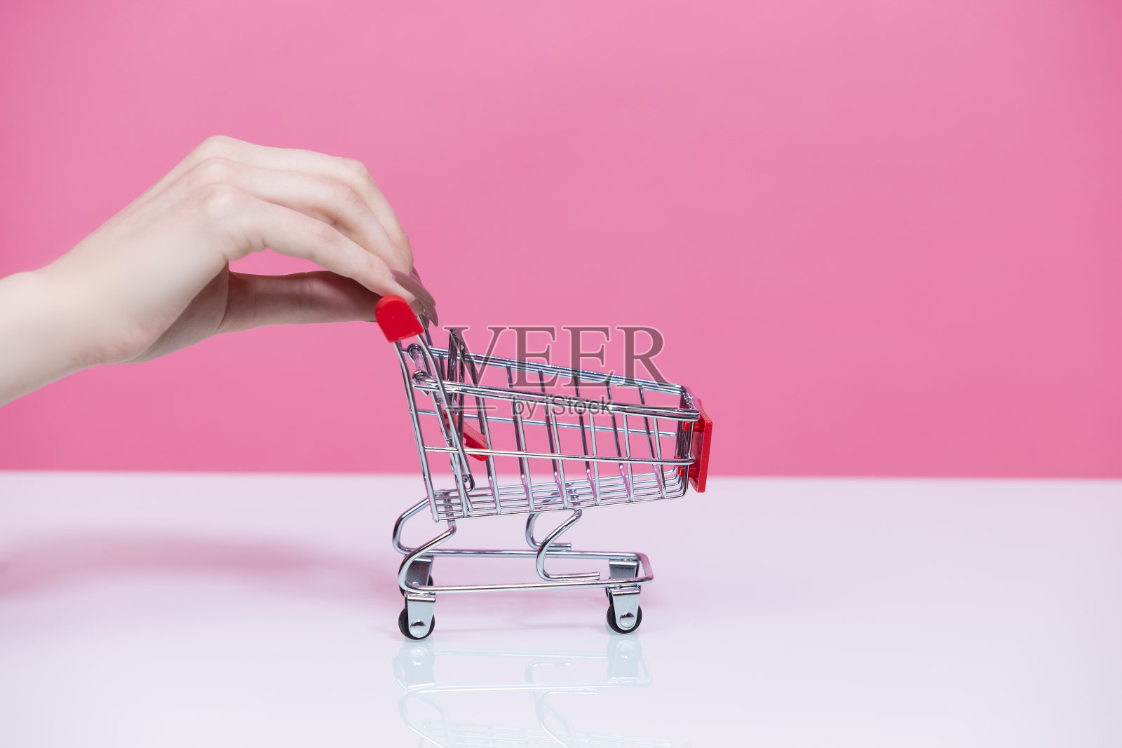 购买的概念。女性手握模型小迷你购物车手推车与双手粉红玫瑰背景。照片摄影图片