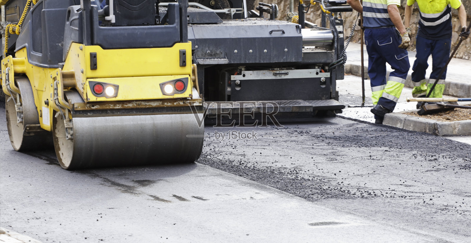 带圆形滚轮的沥青铺路机和穿着制服的操作人员在背景中照片摄影图片