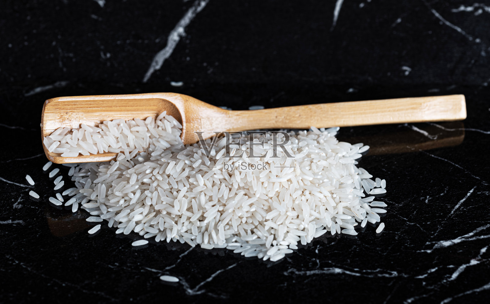 黑色大理石背景上，一堆白米和木勺里的米饭照片摄影图片