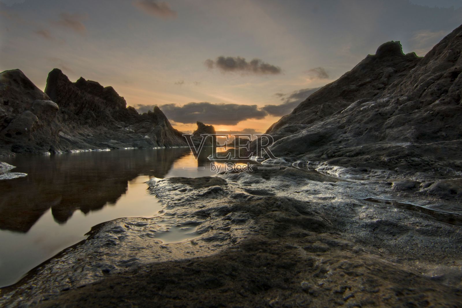 一个平静的岩石隐藏海岸的风景拍摄，金色的傍晚太阳落在云层后面照片摄影图片