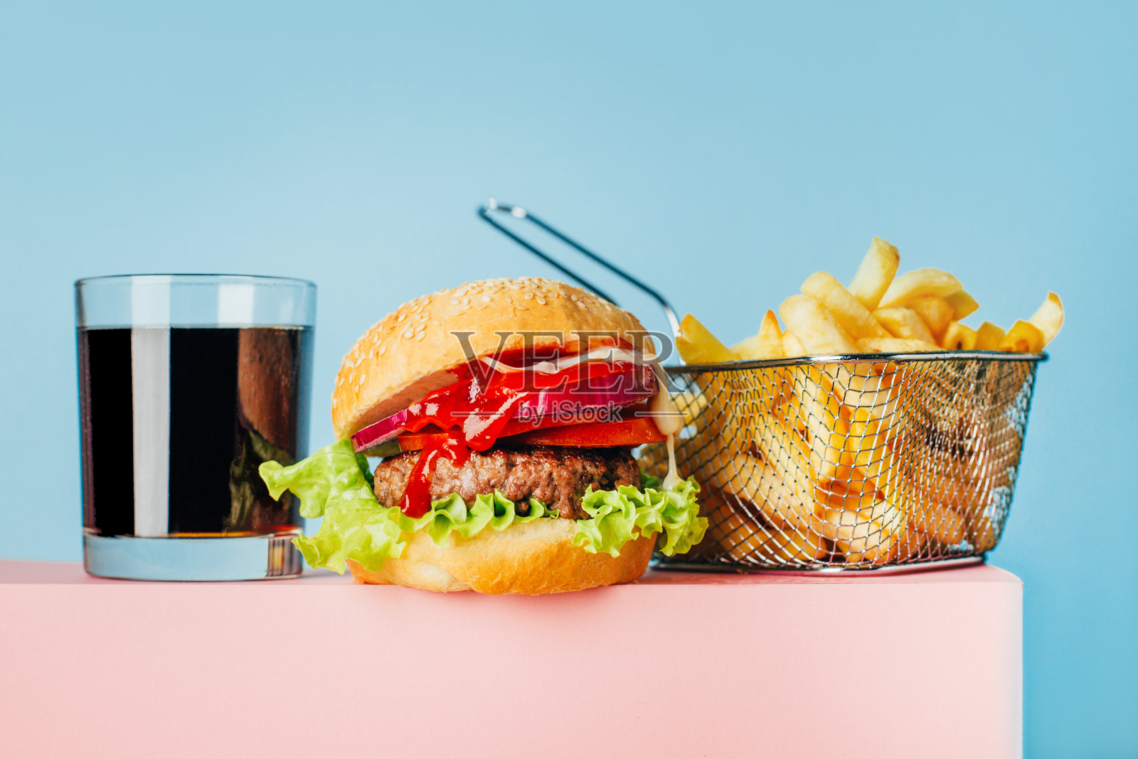 一个汉堡、薯条和苏打水的特写，在一个粉红色的立方体上，蓝色背景上有文本的自由空间照片摄影图片
