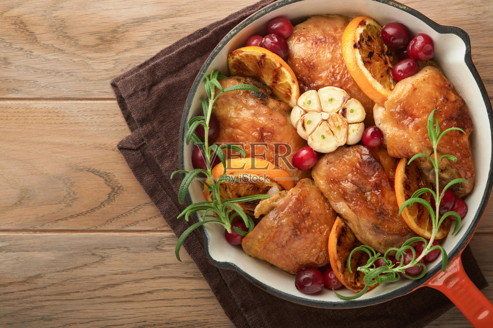 烤鸡腿配橙汁、蔓越莓和香辣香草迷迭香，放在平底锅里，以浅色的木制乡村背景。节日圣诞晚餐概念菜单。前视图。本空间照片摄影图片