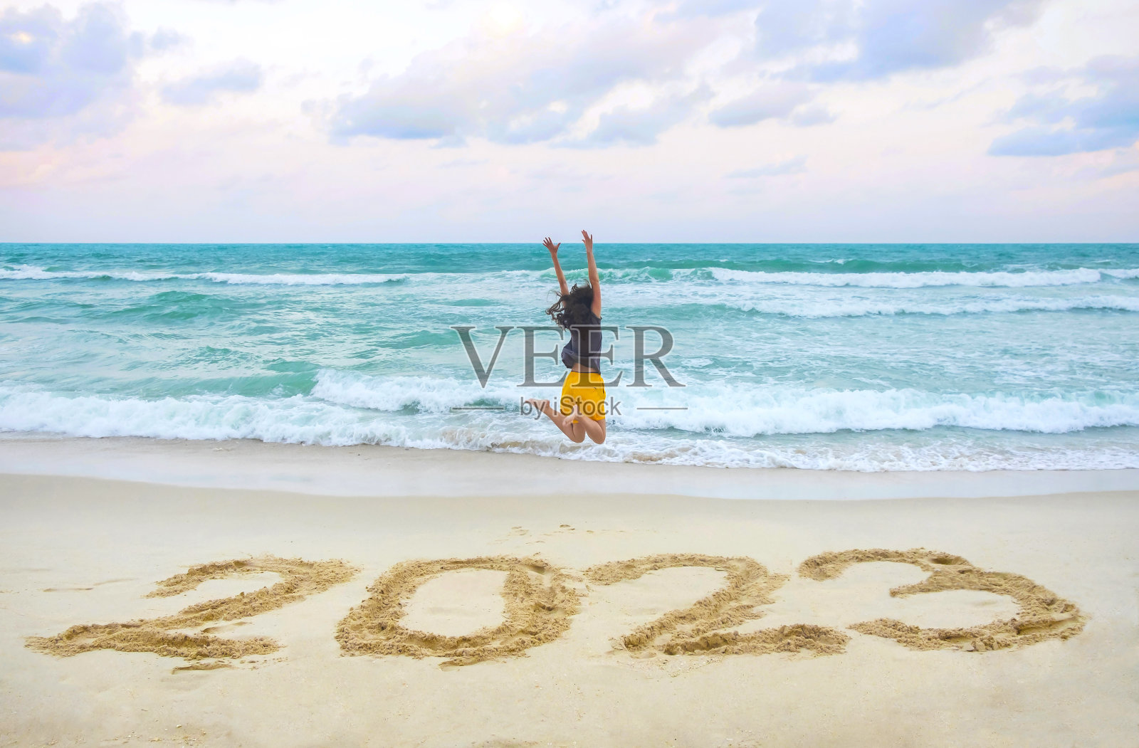 2023年新年在沙滩上，快乐的女人举起双手在沙滩上蹦蹦跳跳照片摄影图片