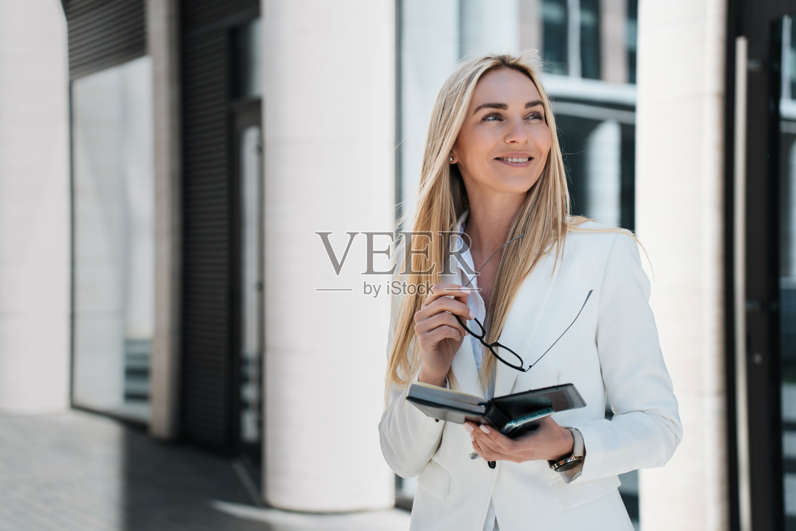 漂亮的瑞典年轻女子在白色西装外面，拿着日记，眼镜，灿烂的微笑，好消息，有目的的经理。经验丰富的商人后，伟大的交易。成功女性照片摄影图片