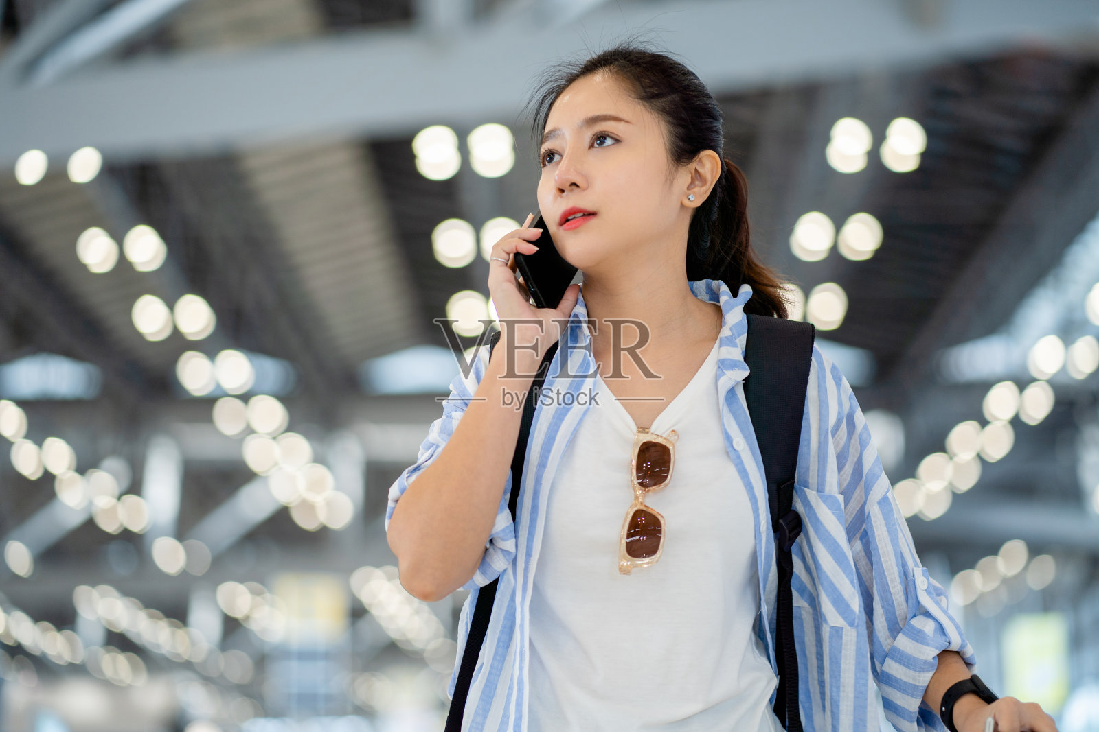 年轻的亚洲女旅客拿着手机在机场预约行李等待航班。照片摄影图片