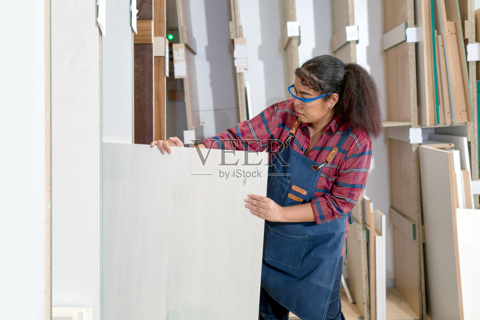 一个中年妇女从储物箱里拉胶合板。亚洲木匠工人在家具厂工作。照片摄影图片