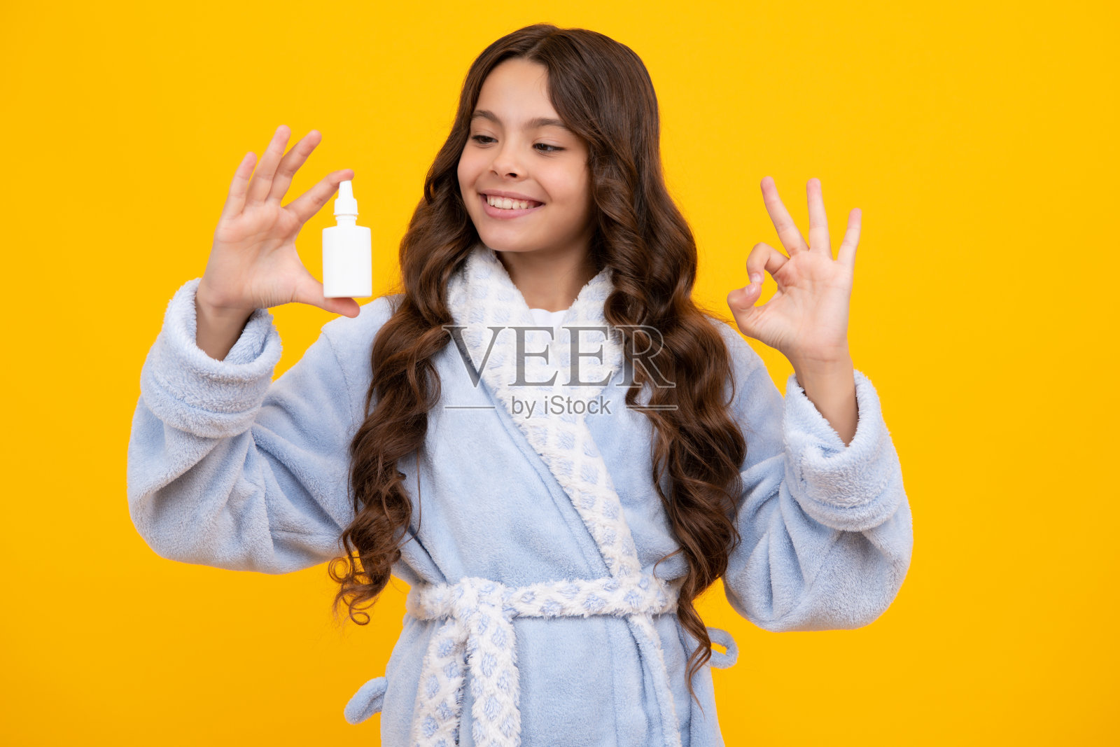 十几岁的女孩拿着药喷鼻从流鼻涕，病毒大流行。黄色背景上有鼻喷雾剂的生病少女。照片摄影图片