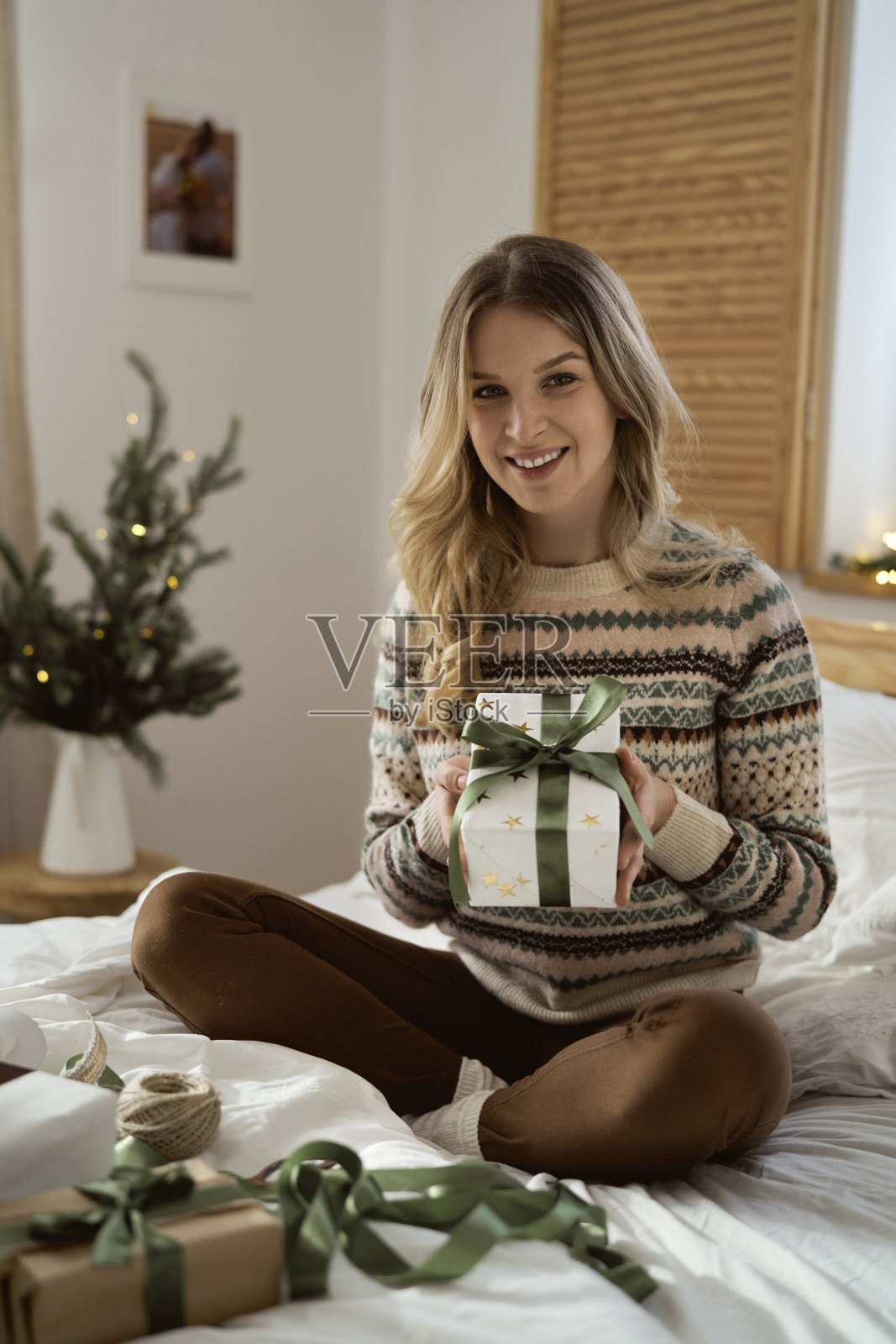 快乐的白人妇女的肖像拿着圣诞礼物，而坐在床上照片摄影图片