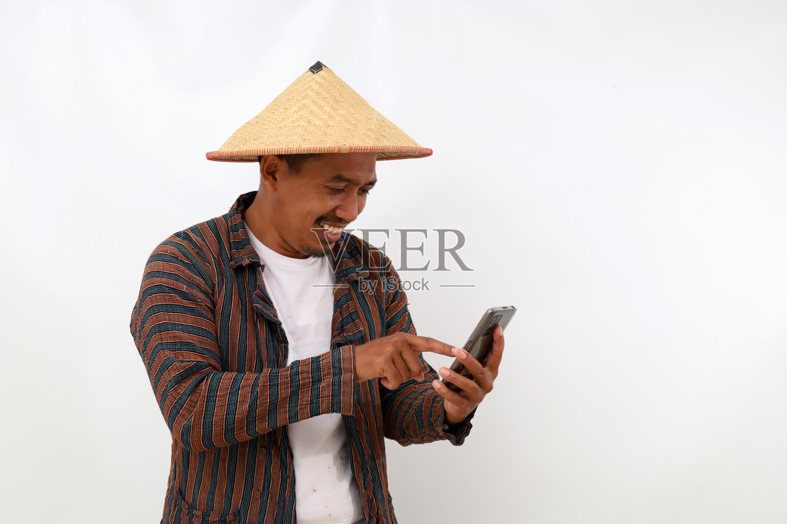 惊讶的亚洲农民站着，拿着并指着手机。隔离在白色背景与复制空间照片摄影图片