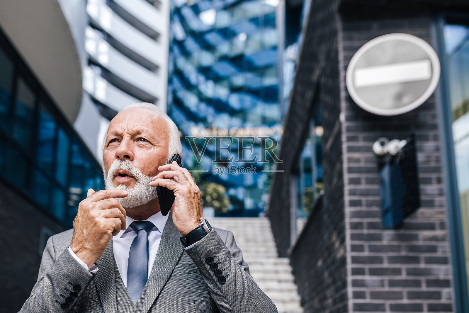 困惑的企业家站在商业办公楼前用智能手机讨论。照片摄影图片