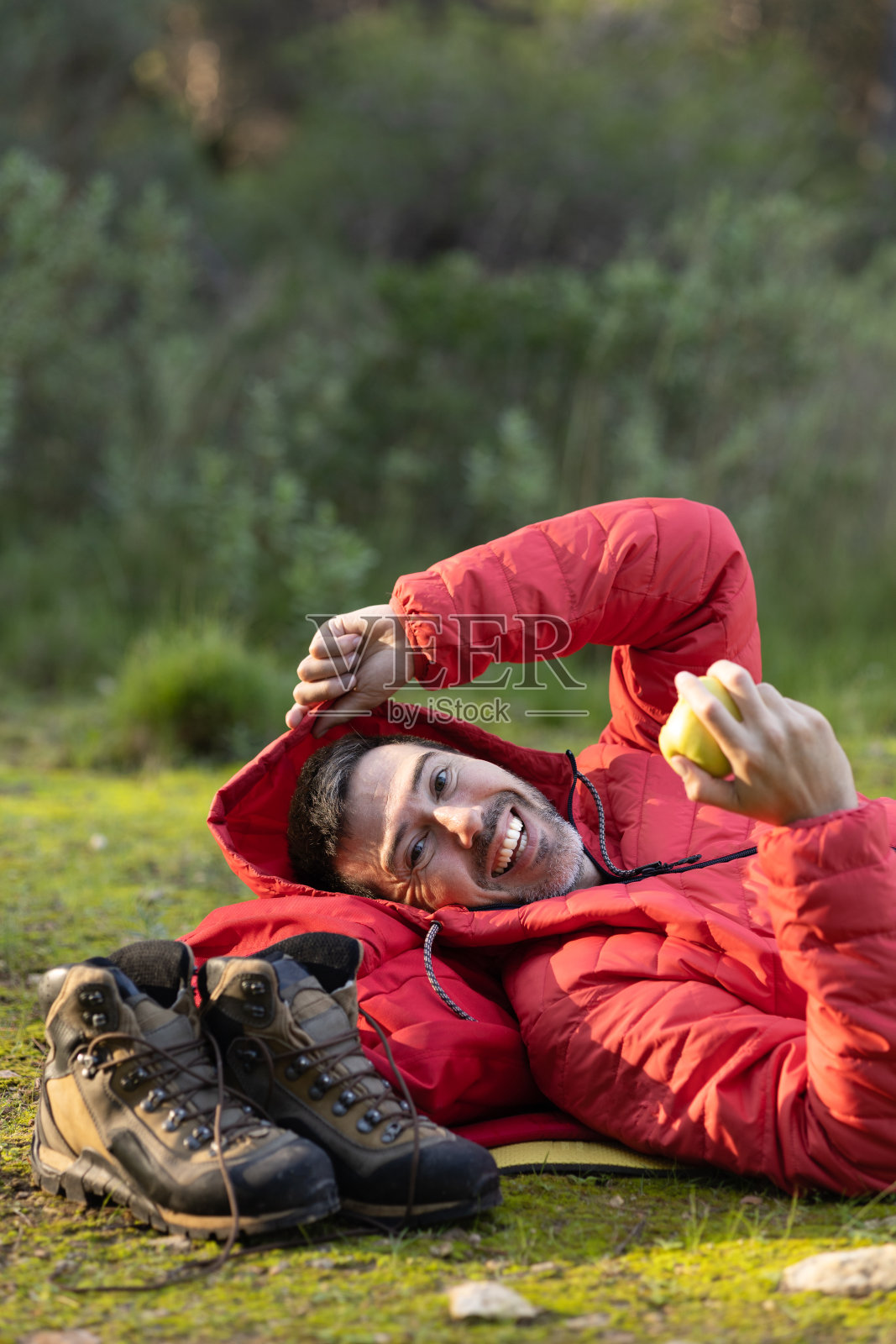 快乐的徒步旅行者微笑着。在一次旅行中，穿着红色夹克和徒步靴，在大自然中吃苹果。照片摄影图片