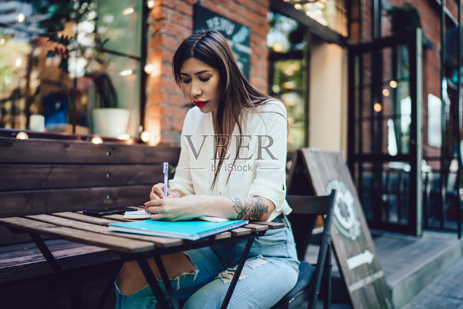迷人的拉丁裔学生坐在咖啡店的咖啡馆露台上，专注于学习过程中撰写大学论文的信息，聪明的学生在户外学习，在教科书上做笔记照片摄影图片