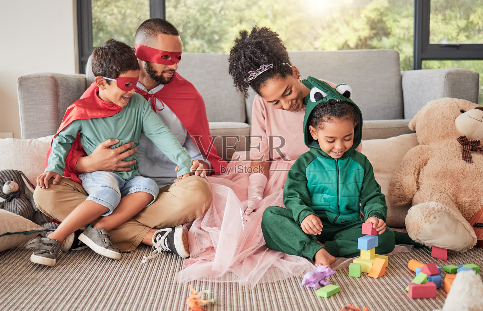 幸福的家庭，超级英雄服装和玩具在客厅，孩子们一起玩，玩得很开心。爱，创意儿童服装万圣节或幻想游戏与关心的爸爸，妈妈和孩子联系。照片摄影图片