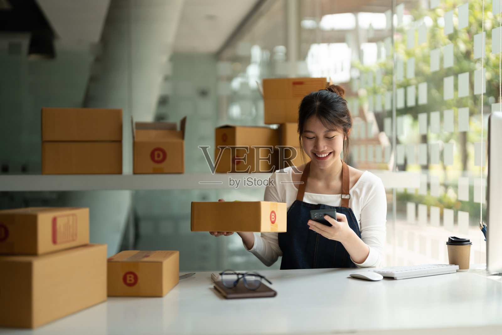 年轻女子小企业主网上购物在家里。用智能手机检查客户订单，后台准备包装产品。中小企业企业家或自由职业者的概念照片摄影图片