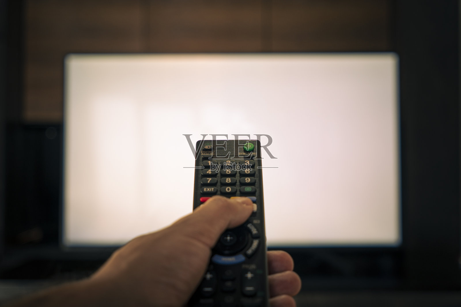 一个男人的手拿着遥控器在一个巨大的白色电视屏幕前。模糊的电视遥控器照片摄影图片