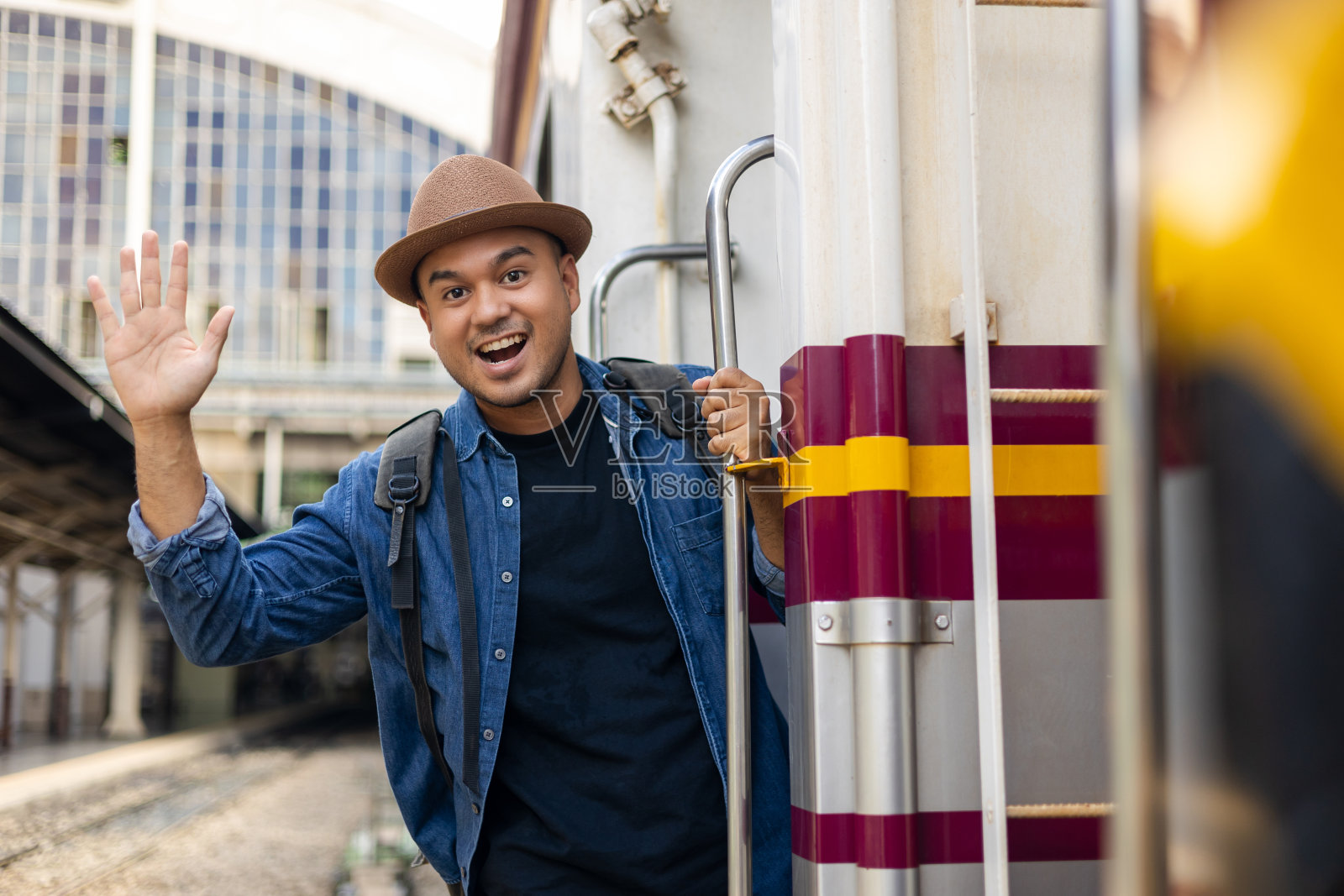 年轻的亚洲男子在开往目的地的火车上悬挂扶手。快乐旅游乘火车旅行假期时间假期周末旅行。男性背包客到达站台。照片摄影图片