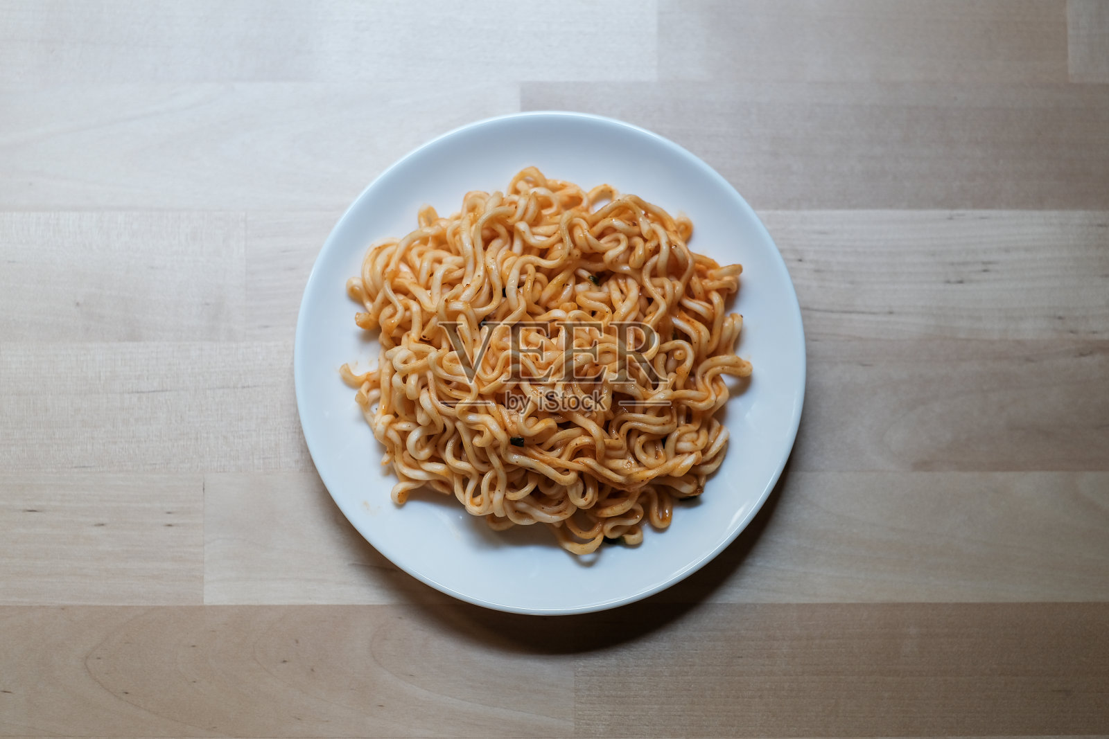 方便面装在一个白色的圆盘子里，放在木桌上照片摄影图片