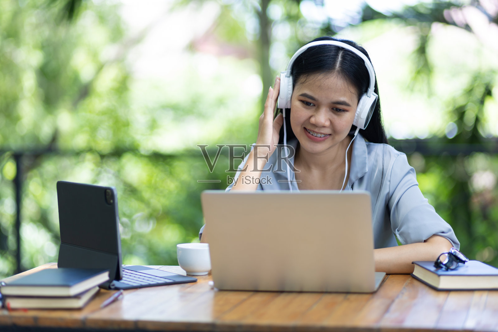 户外商务女士穿着休闲服装，正在笔记本电脑和现代化设备上工作，在自然舒适的环境中，举行网络会议。照片摄影图片